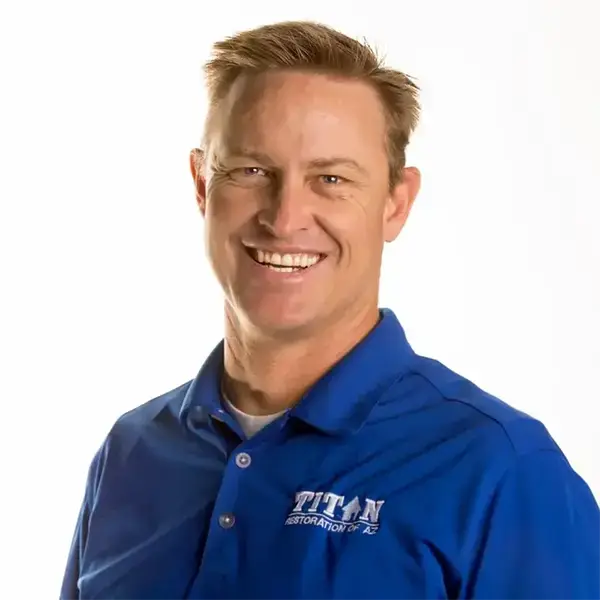 Smiling man wearing a blue Titan Restoration polo shirt against a white background.