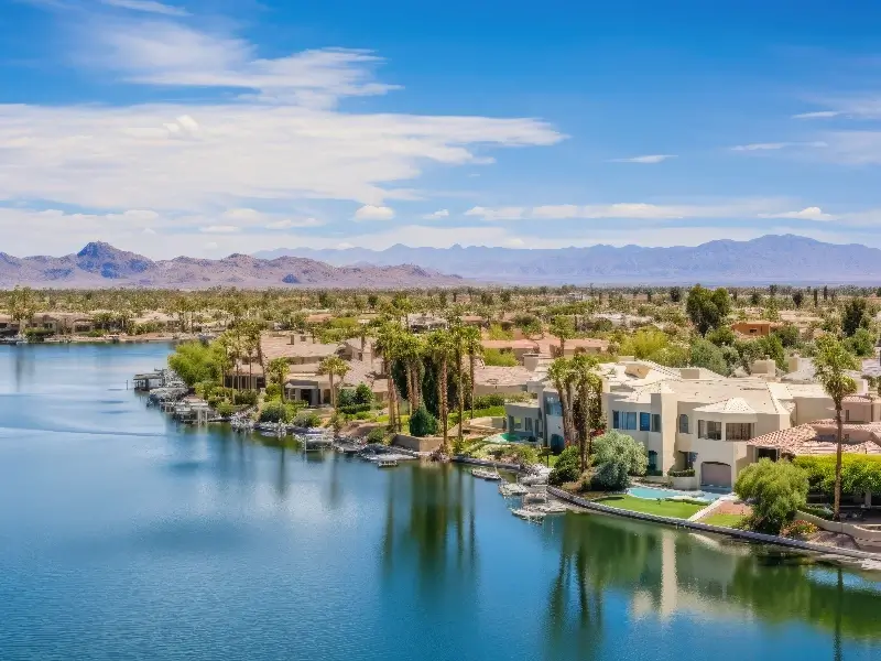Waterfront houses with docks along a calm lake under a blue sky and distant mountains.