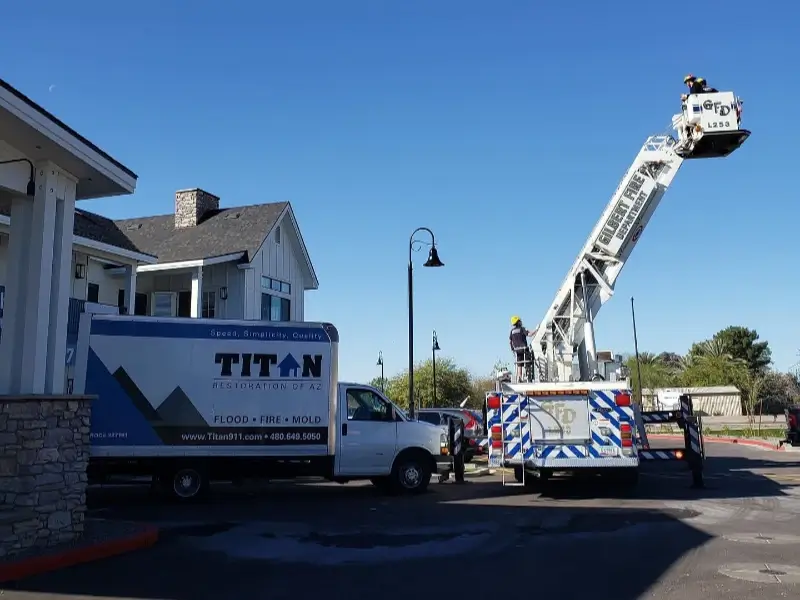 Firefighters on an extended ladder truck near a Titan Restoration service truck outside a building.