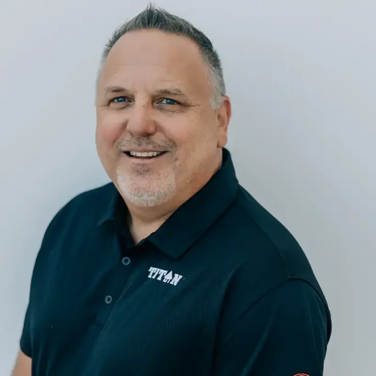 Middle-aged man with short gray hair and goatee smiling, wearing a dark polo shirt with "TITAN" logo.