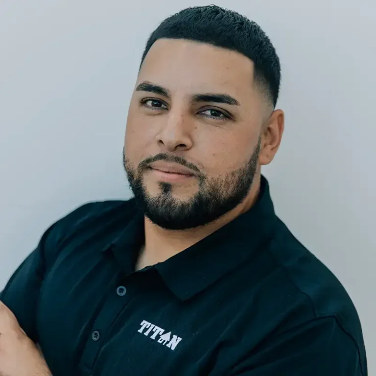 Man with short hair and beard wearing a black shirt with "TITAN" logo, looking at the camera.