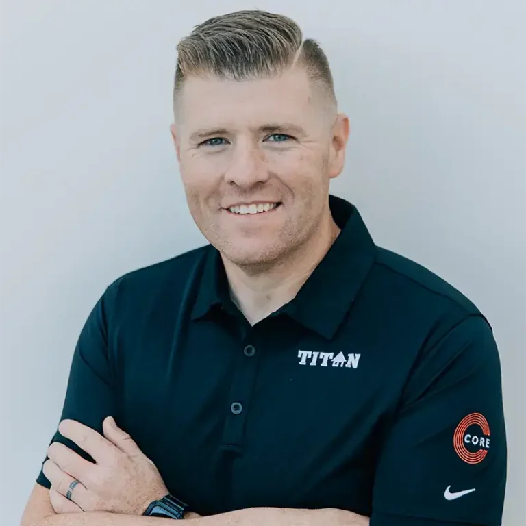 Man with short hair wearing a black Titan polo shirt, smiling with arms crossed.
