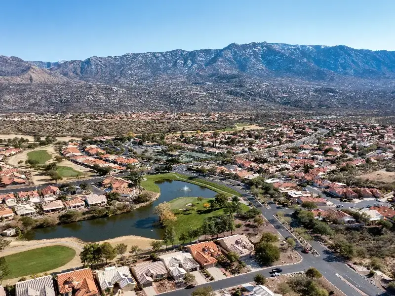 Suburban neighborhood with a small lake and mountain range in the background under a clear sky.