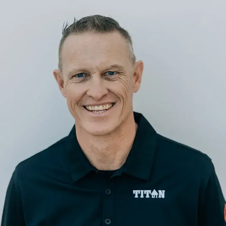 Smiling man with short hair wearing a black shirt with "TITAN" logo on a light background.