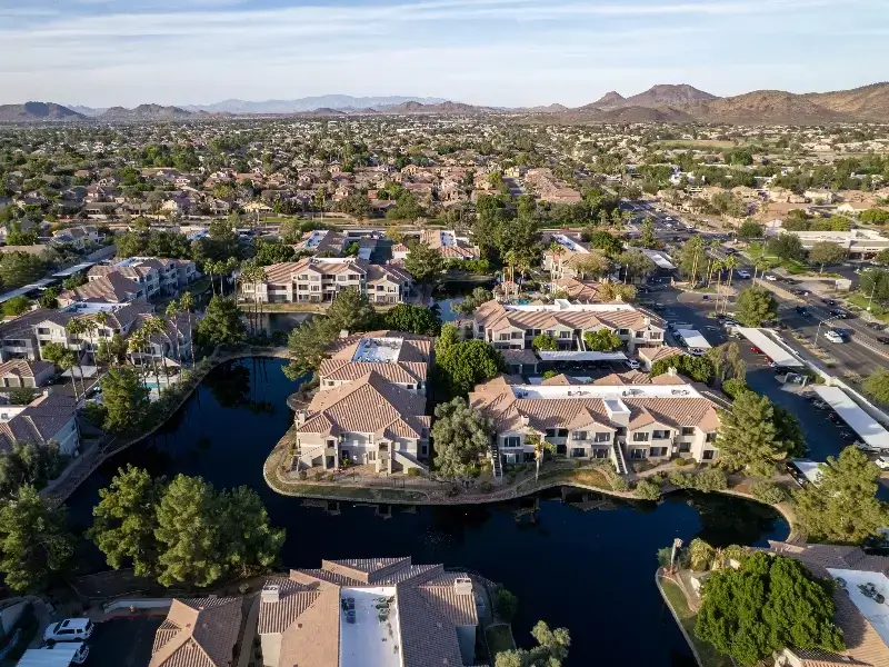 Aerial view of a suburban neighborhood with houses surrounding a water canal and mountains in the background.