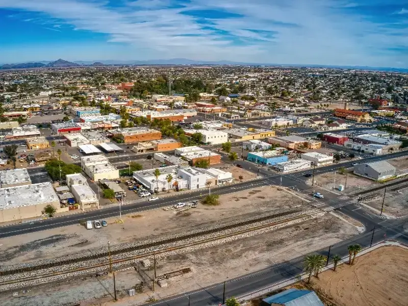 Aerial view of a small city with railroad tracks and roads in the foreground under a partly cloudy sky.