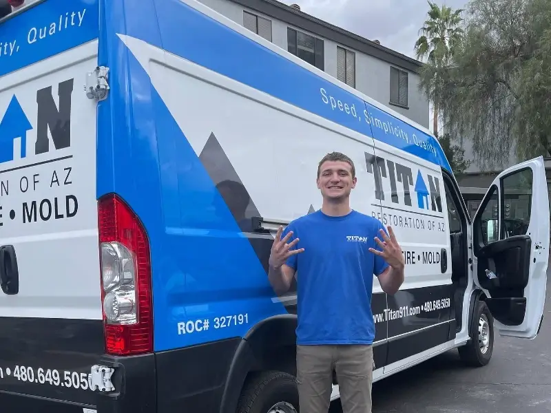 Man in blue shirt standing and smiling in front of a Titan Restoration service van with open door.