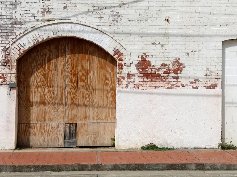 Large wooden arched door set in a white brick wall with peeling paint.
