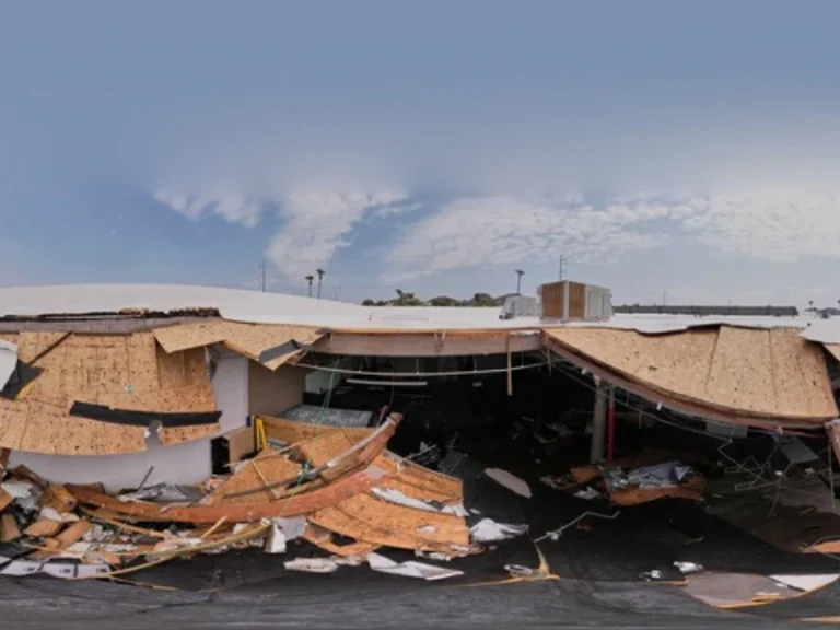 Collapsed roof with scattered wooden debris and exposed interior under a clear sky.