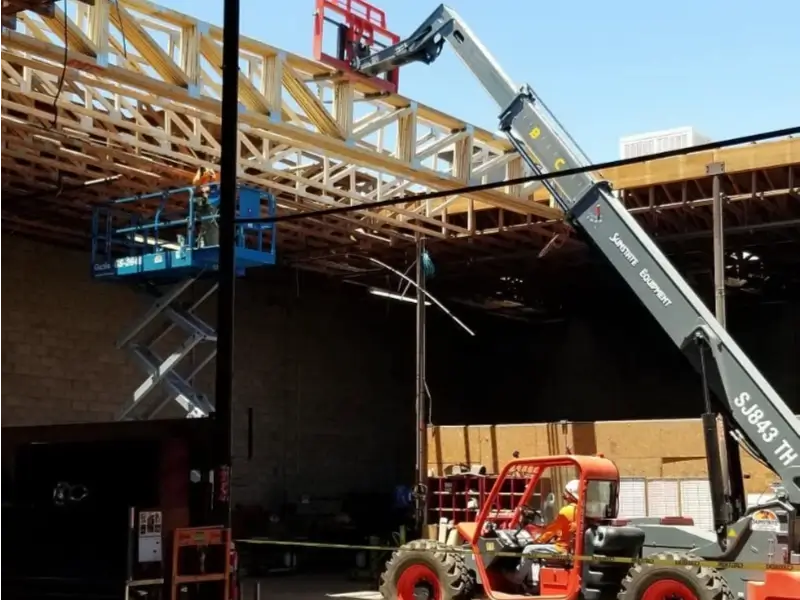 Construction workers operate a scissor lift and a boom lift inside a building under construction.