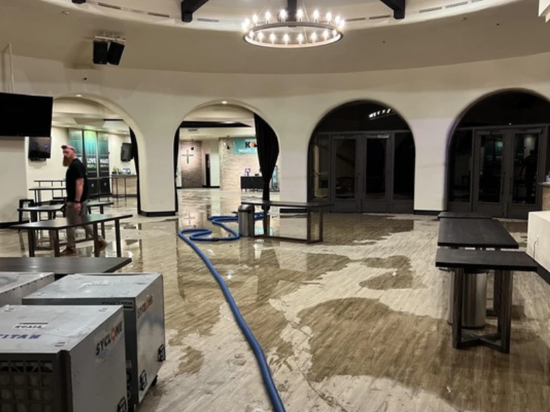 Indoor space with wet floors, tables, and a man walking near a blue hose.