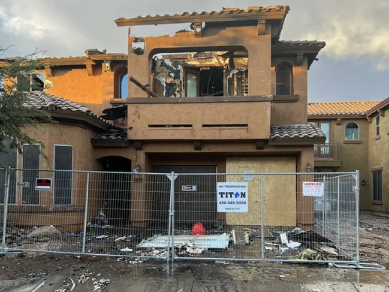 Partially burned two-story house behind a metal fence with warning signs.