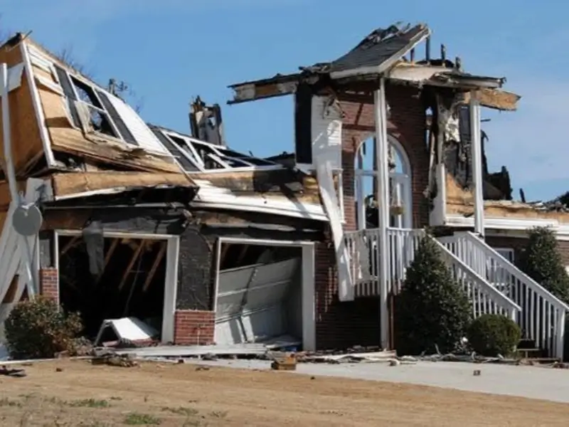 Severely damaged house with collapsed roof and garage, showing extensive fire and structural damage.