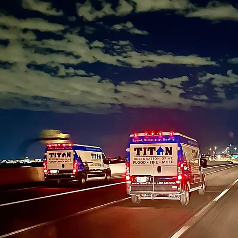 Two Titan Restoration vans driving on a highway at night under a cloudy sky.