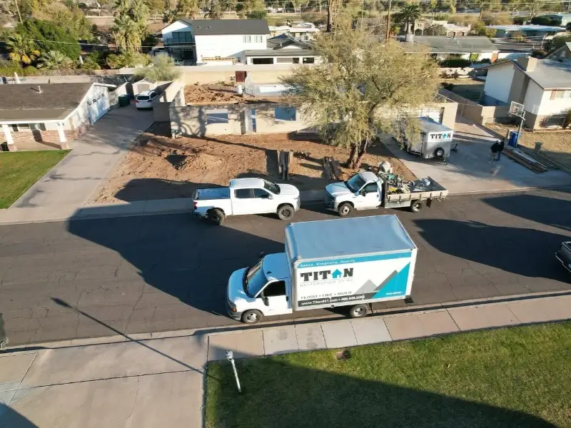 Work trucks parked near a construction site with a partially built house and a large tree.