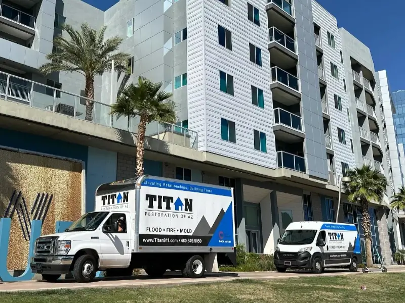 Two Titan Restoration service vehicles parked in front of a modern apartment building with palm trees.