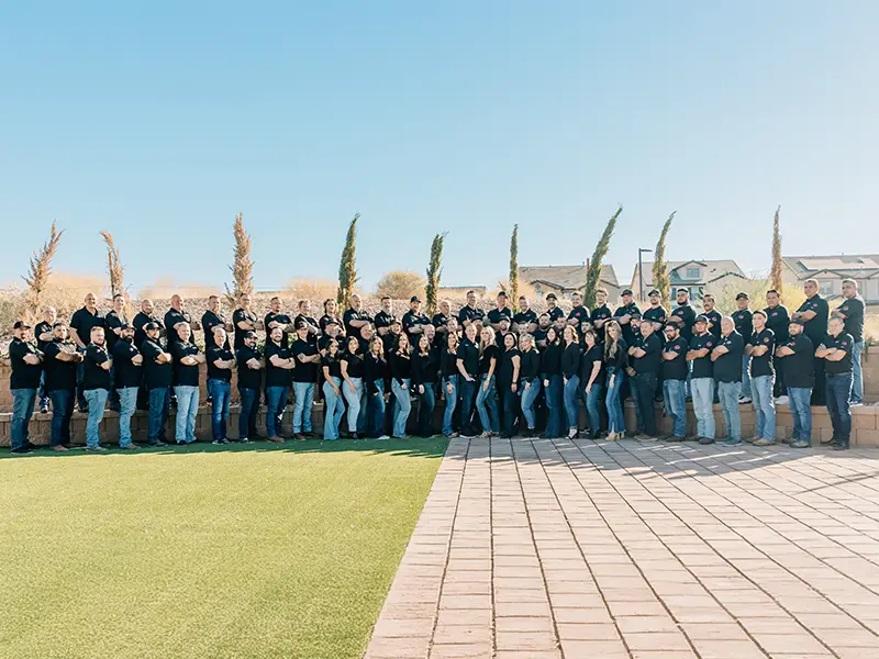 Large group of people standing outdoors in two rows, all wearing black shirts and jeans.