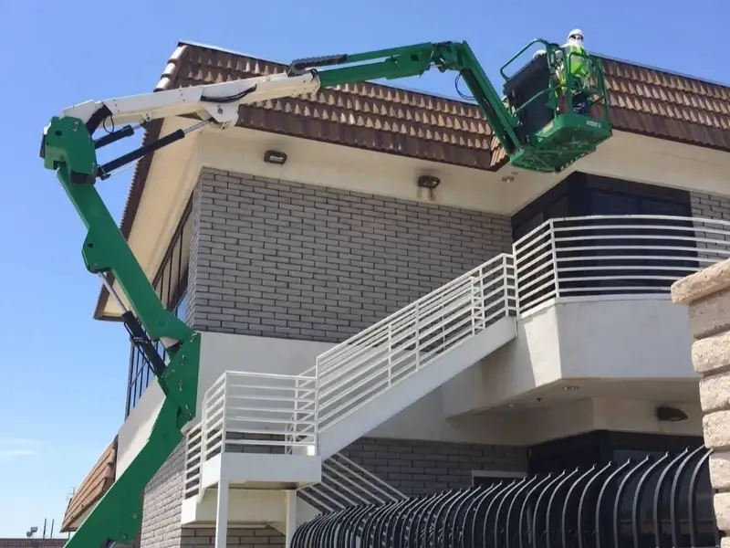 Worker in a green aerial lift inspecting the exterior of a two-story building.