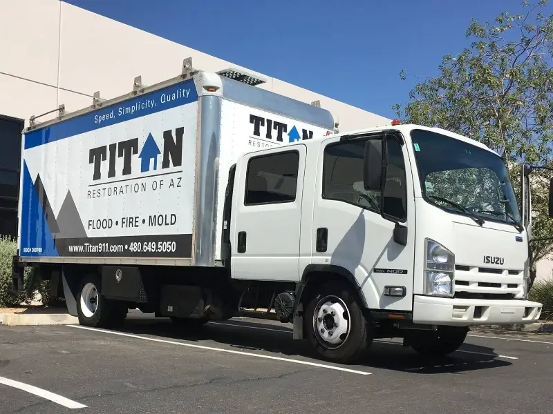 White Isuzu box truck with Titan Restoration of AZ branding parked outside a building.