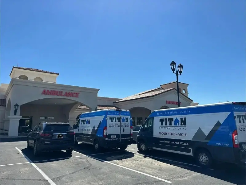 Two Titan Restoration service vans and a black SUV parked outside a hospital emergency entrance.