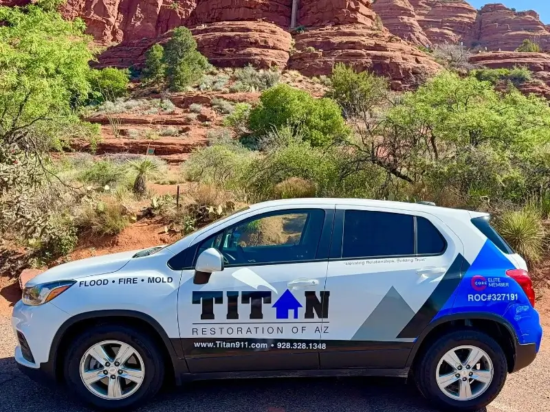 White SUV with Titan Restoration of AZ logo parked in front of red rock formations and green shrubs.