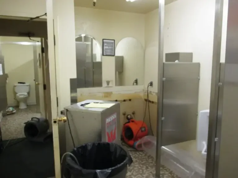Restroom under maintenance with drying equipment, trash can, and open toilet stall visible.