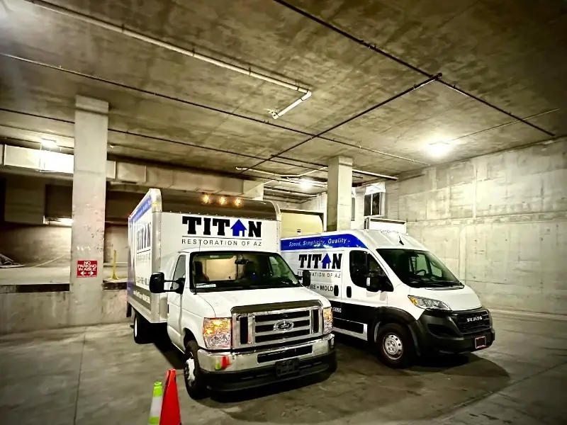 Two white Titan Restoration service vans parked inside a concrete garage.