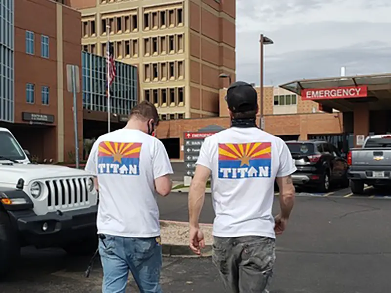 Two men wearing white Titan shirts walk toward a hospital emergency entrance.